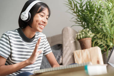 亞洲女孩通過平板電腦上的網(wǎng)絡(luò)導(dǎo)師在網(wǎng)上揮手致意，亞洲孩子則坐在客廳里曬太陽，一邊學(xué)習(xí)和問候早上好的老師。在家學(xué)習(xí)概念