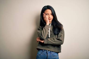 年轻而漂亮的中国女运动员，身穿运动衫，披着孤立的白色背景，满脑子疲惫不堪，双手交叉，对抑郁症感到厌烦