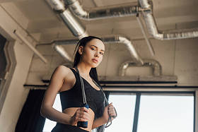 带跳绳的漂亮女运动员在体育馆看相机时的低视角