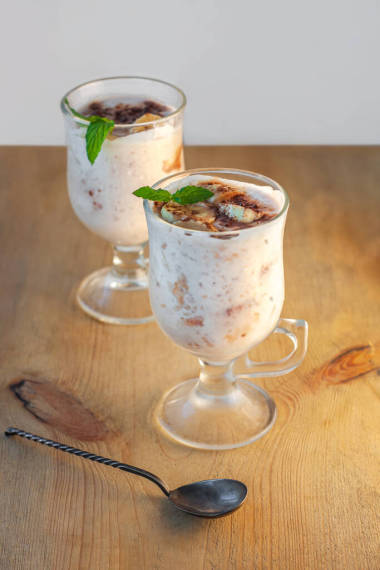 含香蕉、草莓、可可、新鮮薄荷的酸奶果凍配香蕉、草莓、可可、新鮮薄荷糖在木制切菜板上的杯子里。健康的自制甜蔬菜食物。香草瓊脂牛奶布丁低熱量食譜，垂直橫幅