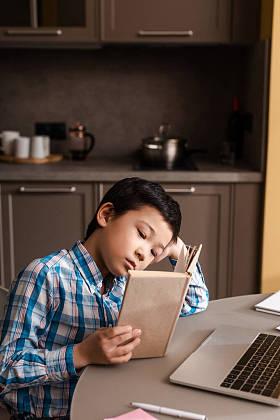 在自我隔离期间，亚洲小孩在家里看书，带着笔记本电脑上网学习