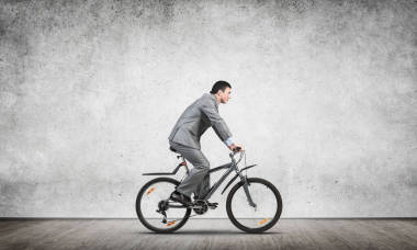 商人騎自行車上下班.穿西裝的人騎自行車.灰色墻壁后面的英俊的騎車人.生態(tài)友好型交通和生活方式。就業(yè)和職業(yè)發(fā)展