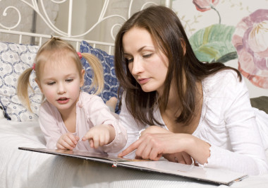 幸福的家庭、 母親和女兒躺在床上看書，聊天的肖像