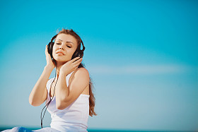 美丽的女人，听听音乐耳机在海边蓝天的衬托