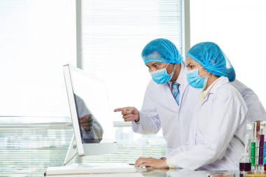 戴口罩的越南实验室工作人员讨论电脑屏幕上的研究细