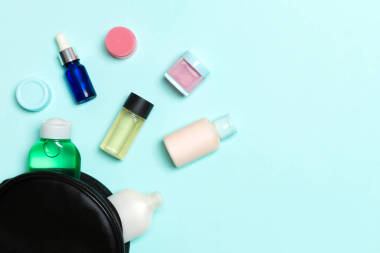 在蓝色的背景下，一群化妆品瓶子从化妆品包里掉了出来。空间为您的设计。护肤概念的最高视图