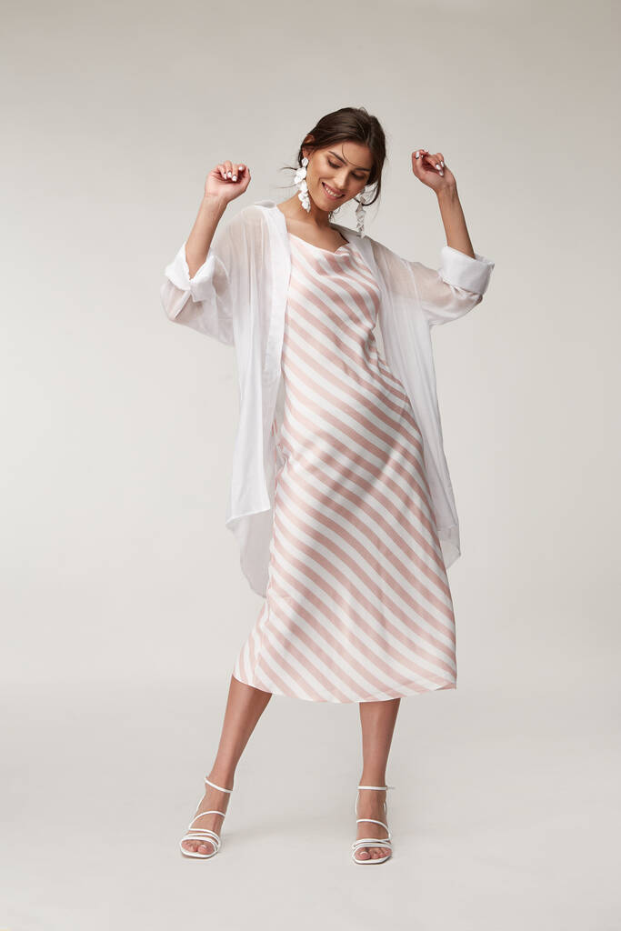 性感的时尚模特美女漂亮的脸蛋妆容，晒黑的皮肤穿夏季系列服装浪漫的约会风格走着时髦的浅色丝绸在白色粉红条纹长裙白衬衫耳环