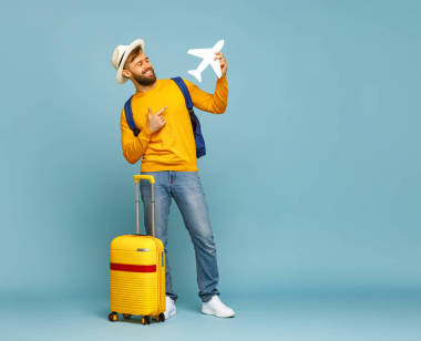 全身上下喜怒無常的男人笑著指著玩具飛機(jī)，站在藍(lán)色背景的行李旁邊