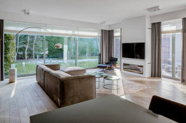 雅致的客廳，有時尚家具、木制地板、深色餐桌和有花園景觀的窗戶墻