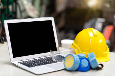 工业中的防护和安全设备及笔记本电脑.车间安全事故用黄色安全帽、安全护目镜和带手提电脑的卫生面具