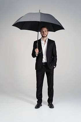 穿着西服站在黑色雨伞下的商人