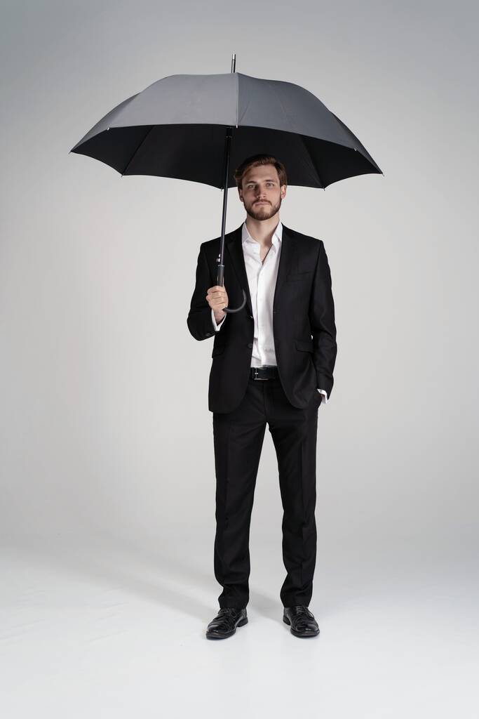 穿着西服站在黑色雨伞下的商人