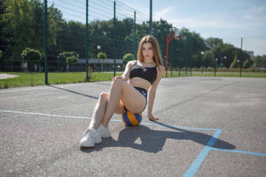 在室外長發(fā)的年輕女運動員坐在操場上拿著一個球