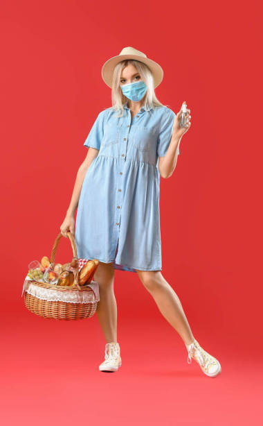 帶著防護(hù)面罩和食物的年輕女子，穿著彩色背景的籃子野餐
