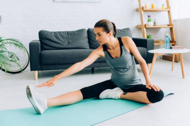 年轻孕妇坐在健身垫上做伸展运动