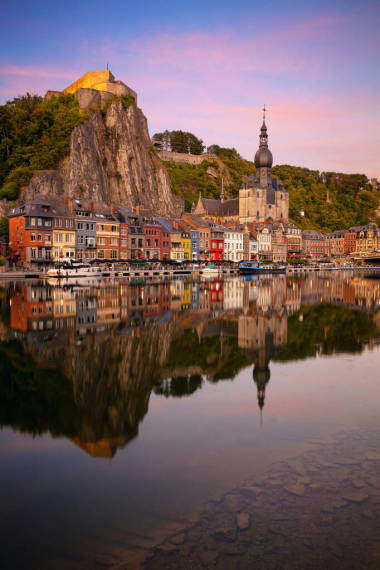  比利时，迪南美丽的历史名城迪南的城市景观形象与夏季日落时默兹河中的城市倒影