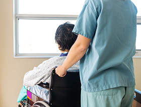 坐在轮椅上同时护士协助他在窗的病人