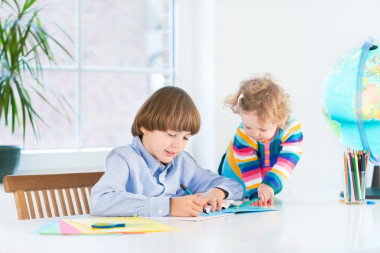 學(xué)校男孩做他的作業(yè)，他蹣跚學(xué)步的姐姐看著他