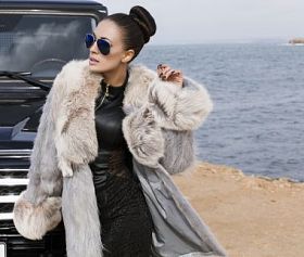 在一辆车旁边摆姿势的毛皮大衣的性感魅力女人