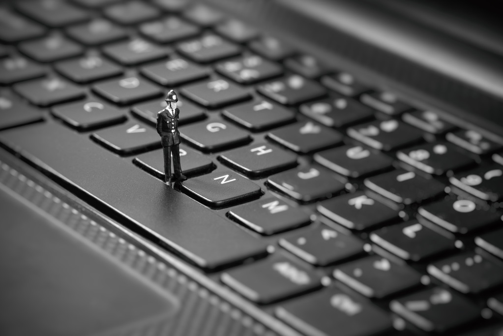 检查笔记本电脑的小型警察。盗版、 互联网黑客概念 检查笔记本电脑的小型警察。盗版、 互联网黑客概念