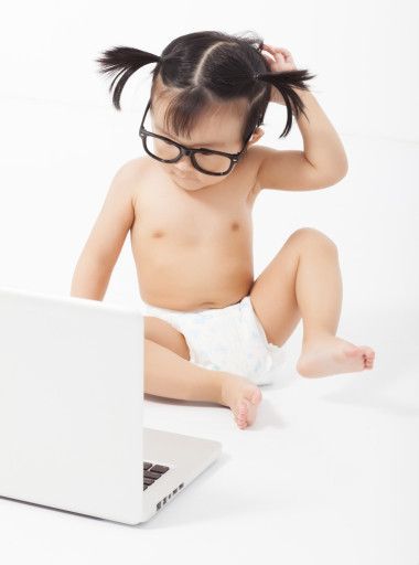 小孩坐在一臺(tái)筆記本電腦上玩。白色襯底上分離