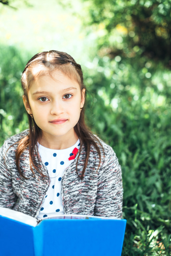一个可爱的年轻女孩读一本书的室外肖像