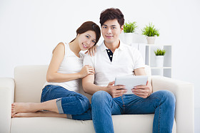 快乐的年轻夫妇，在沙发上的平板电脑 