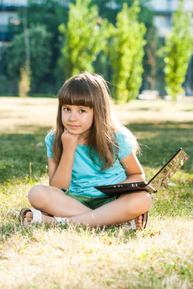 漂亮的小女孩坐在她的笔记本上公园