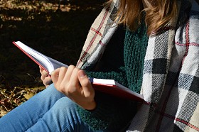 年轻、 漂亮的女孩裹在温暖的格子毛毯，喝热茶和读一本书在公园