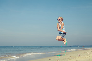 少女在夏天 vaca 的藍(lán)色的大海岸邊沙灘上跳躍
