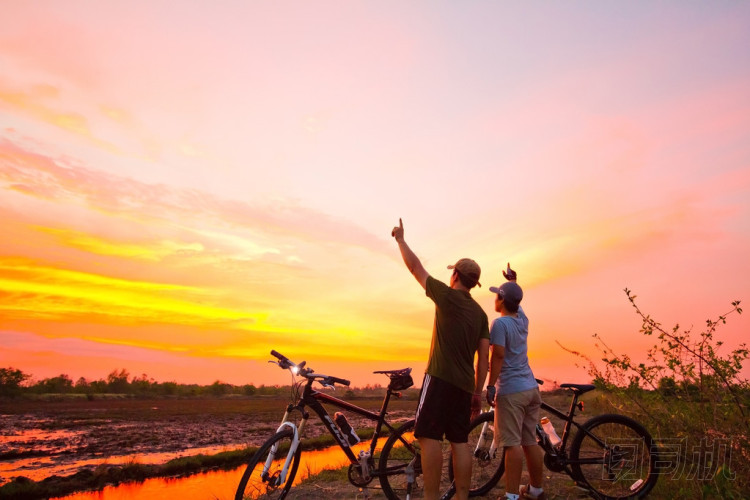 后方的看法的一個年輕男人站在日落時與一輛自行車。治愈