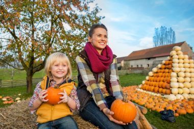幸福的母親和孩子坐在干草堆里用南瓜