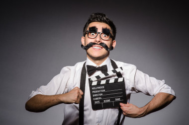 假胡子持有 clapperboard 上孤立的年輕男人