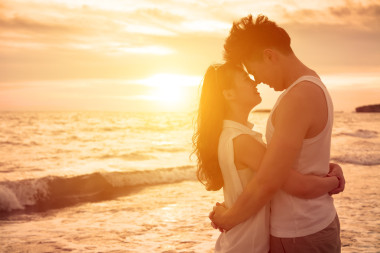 年輕的夫婦在海灘上在日落時接吻