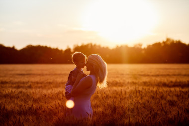 妈妈和儿子在湖边，外地在户外享受大自然的乐趣。在晴朗的天空上的剪影。温暖的筛选器和电影效果