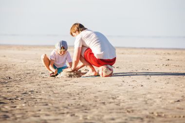 快樂的父親和兒子在夕陽光在海灘上玩很開心