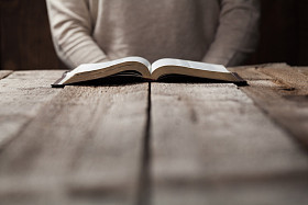 Woman reading the Bible in the dark at a wooden table
