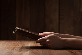 Woman reading the Bible in the dark at a wooden table