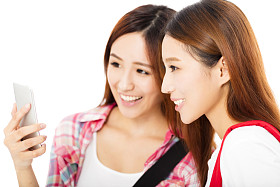 看着智能手机的两个快乐的青少年学生女孩