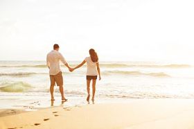 在日落时在沙滩上散步的情侣照片