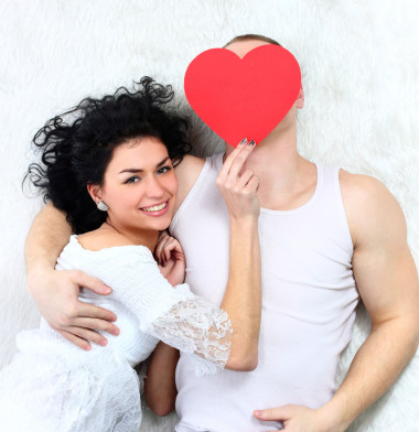 可愛(ài)的情侶舉行紅色的心在一起躺在床上