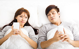 快乐的年轻夫妇，在一张床，智能手机
