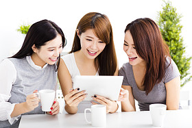 三个快乐的年轻女子看在客厅里的平板电脑
