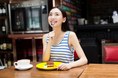 美麗的年輕女子坐在和吃蛋糕圖片