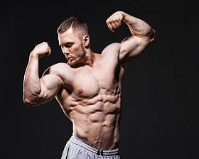 肌肉赤膊男工作室在黑暗的背景中显示他的肌肉