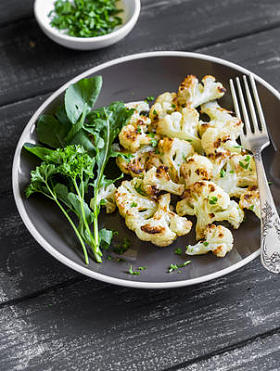 烤花椰菜和棕色黑色木制背景板上的新鲜绿色沙拉