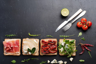 在黑板上放上各種澆頭如芝麻菜藍(lán)奶酪番茄干梨片火腿等的三明治