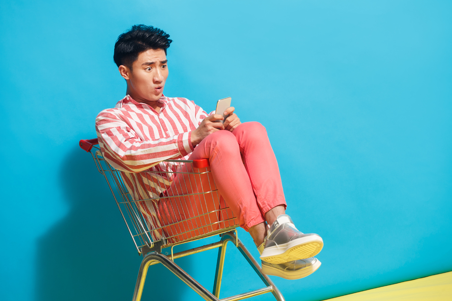青年男人坐在购物车里看手机 青年男人坐在购物车里看手机