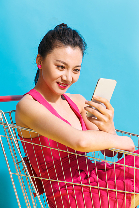 青年女人坐在购物车里看手机