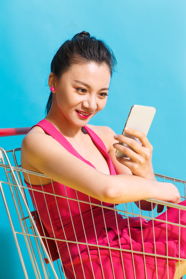青年女人坐在购物车里看手机 青年女人坐在购物车里看手机
